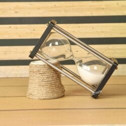 The modern white sand hourglass used as a decorative piece, leaning against a rustic table accessory.