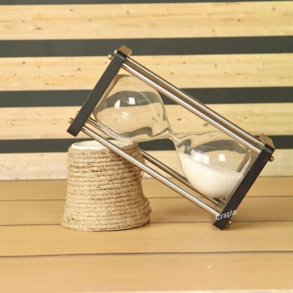 The modern white sand hourglass used as a decorative piece, leaning against a rustic table accessory.