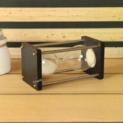 The 5-minute white sand hourglass lying on its side on a wooden surface, displaying its modern design.