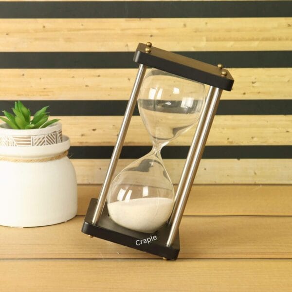 The 5-minute black wood and nickel brass hourglass displayed at an angle next to a decorative plant.