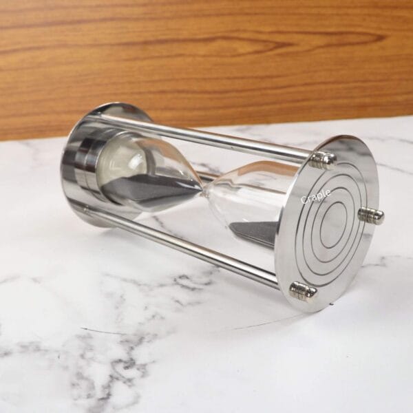 The nickel and brass sand timer lying on its side, showing the sturdy pillar construction and black sand.