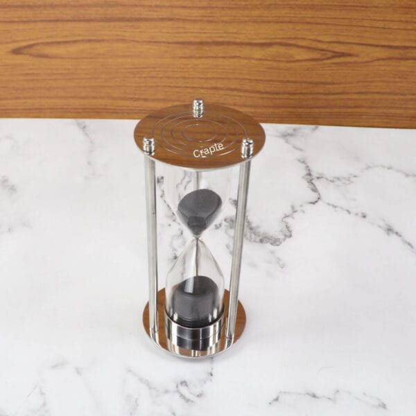 A 5-minute hourglass with black sand, featuring a polished nickel base and pillars with a contrasting wooden top.