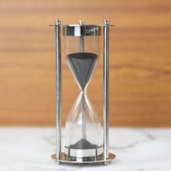 A modern 5-minute hourglass with a full nickel finish, featuring a sleek frame, black sand, and sturdy pillars.