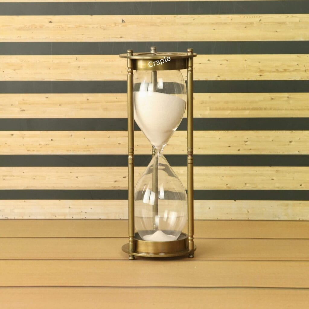 A tall, 60-minute hourglass with white sand, housed in a vintage-style antique brass frame.