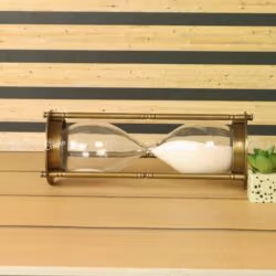 The tall white sand hourglass lying on its side, showing the glass bulb and antique brass pillar construction.