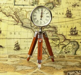 A vintage-style desk clock with a nickel finish and Roman numerals, mounted on an adjustable wooden tripod stand.