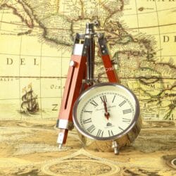 The round nickel clock detached from its stand, resting beside the folded wooden tripod legs on a map.
