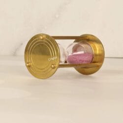 The brass and pink sand hourglass lying on its side, highlighting its sturdy pillar construction.