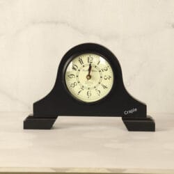 A classic black antique wooden desk clock with an arched top and a vintage-style off-white dial with Arabic numerals.