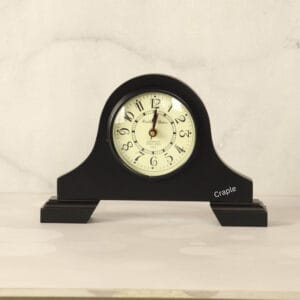 A classic black antique wooden desk clock with an arched top and a vintage-style off-white dial with Arabic numerals.