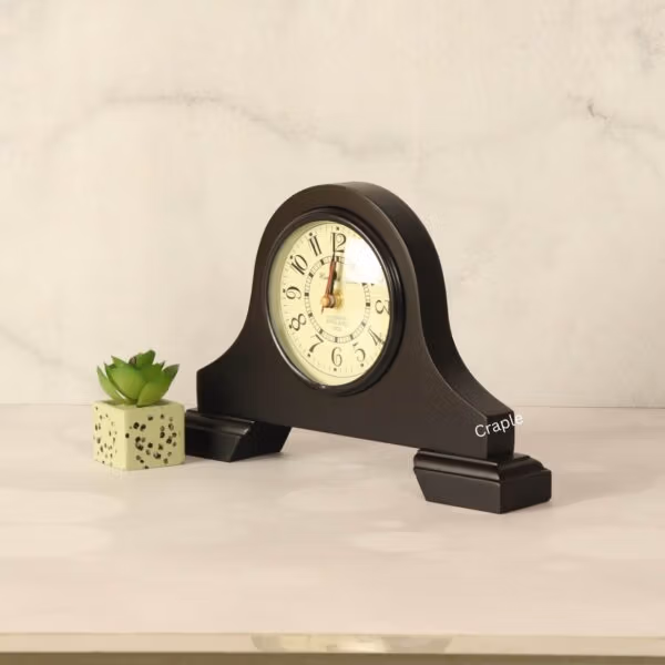 Angled view of the black wooden mantel clock, showcasing its classic shape as a decorative accessory next to a plant.