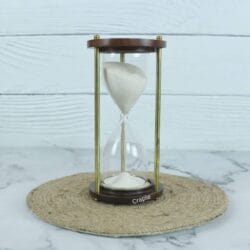A classic handmade 3-minute sand timer with white sand, framed by dark wooden bases and shiny brass pillars.