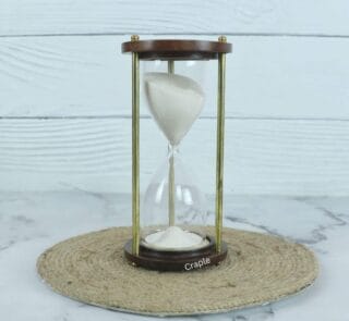 A classic handmade 3-minute sand timer with white sand, framed by dark wooden bases and shiny brass pillars.