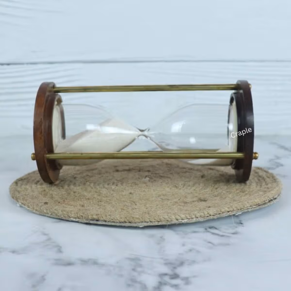 The handmade wooden and brass sand timer resting horizontally on a jute coaster, showing the white sand.