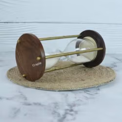 The white sand hourglass viewed from the side while lying down, focusing on the wooden and brass frame.