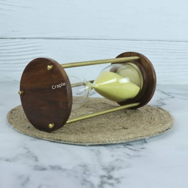 The yellow sand hourglass lying on its side, highlighting the contrast between the dark wood and the golden brass pillars.