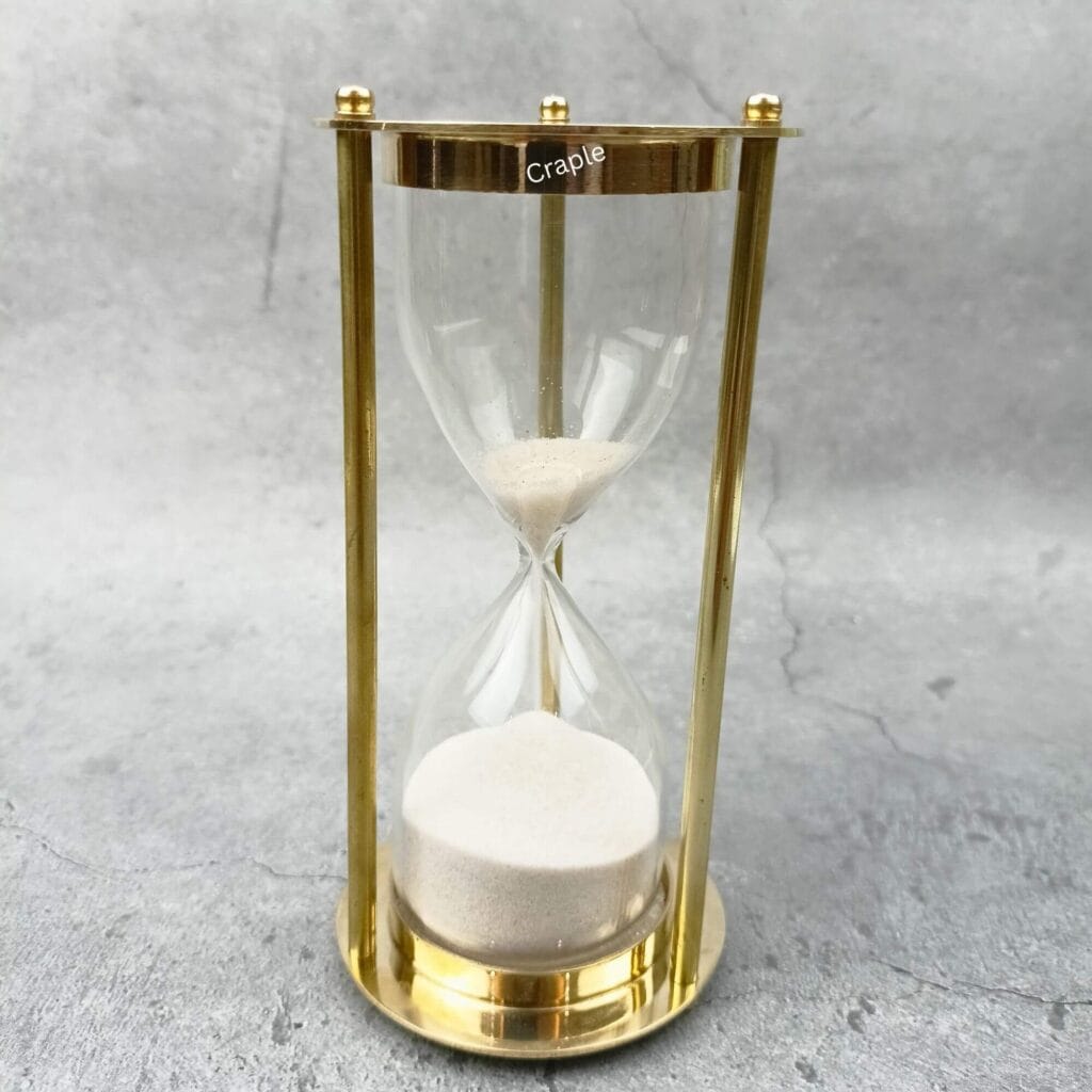 An elegant 5-minute hourglass with a shiny brass frame, three pillars, and fine white sand.