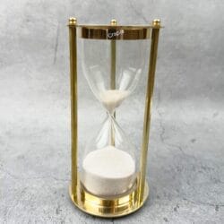 An elegant 5-minute hourglass with a shiny brass frame, three pillars, and fine white sand.