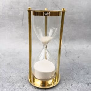 An elegant 5-minute hourglass with a shiny brass frame, three pillars, and fine white sand.