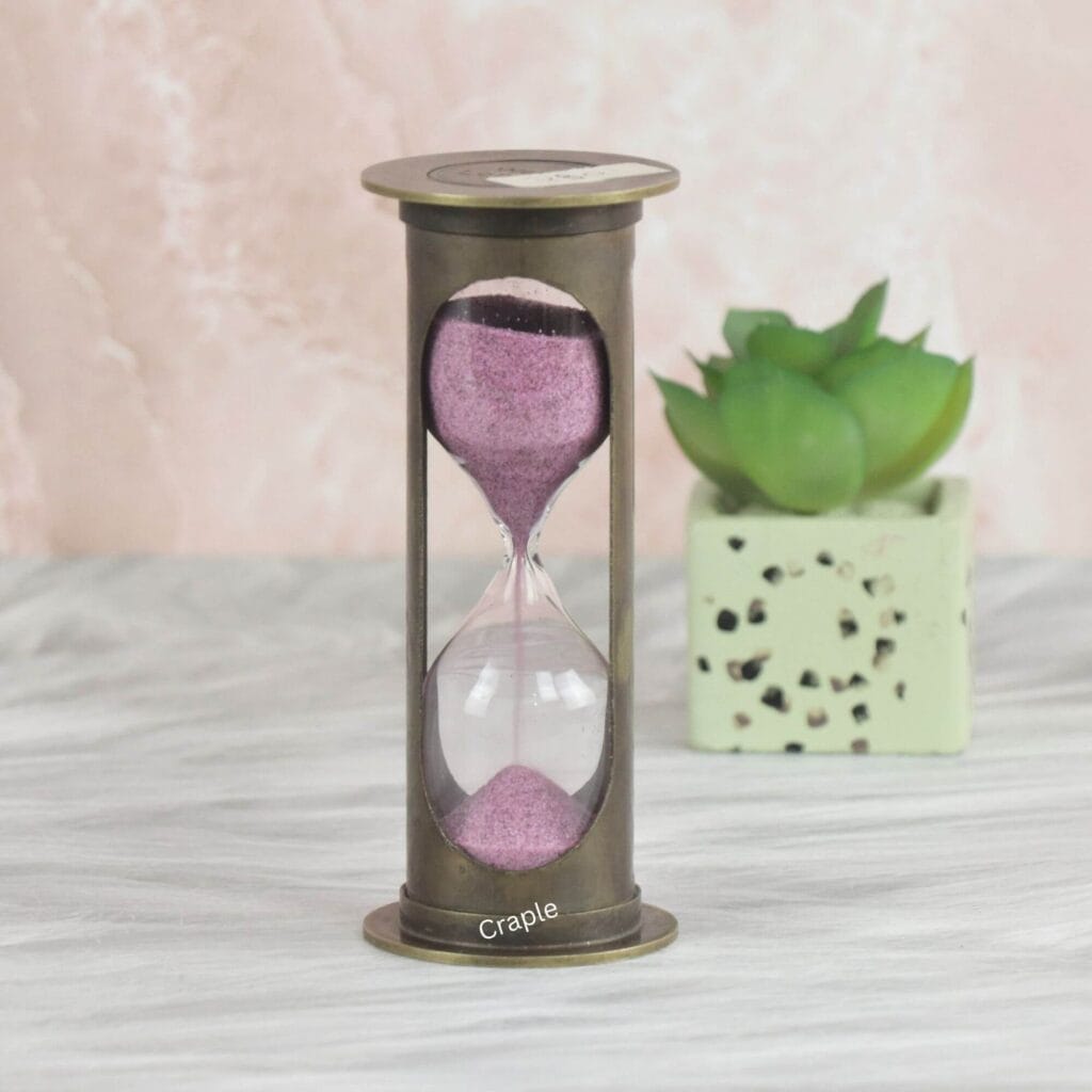A vintage-style 1-minute hourglass with a cylindrical antique brass frame and sparkling pink sand.