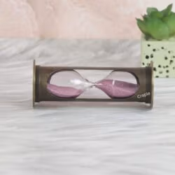 The cylindrical antique brass sand timer resting horizontally, showcasing the glass and pink sand inside.