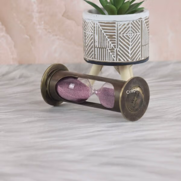 The antique brass 1-minute hourglass used as a decorative desktop accessory with a plant.