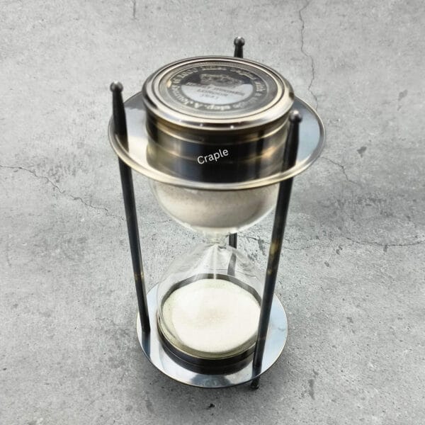 A 5-minute hourglass sand timer with a black antique brass frame and a built-in compass on top.