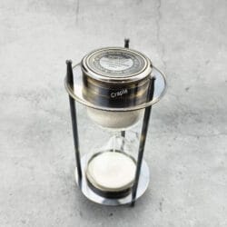 High-angle view of the vintage-style sand timer, showing the compass face and white sand.