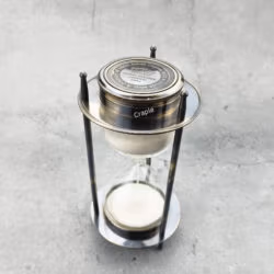 High-angle view of the vintage-style sand timer, showing the compass face and white sand.