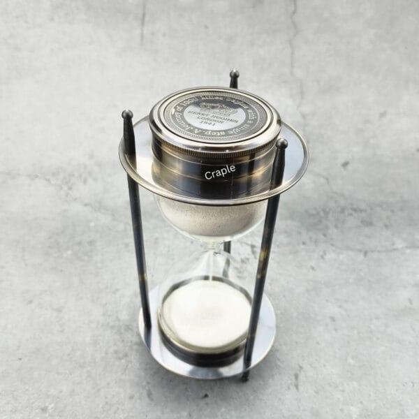 High-angle view of the vintage-style sand timer, showing the compass face and white sand.