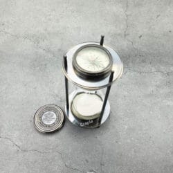 The black antique brass sand timer with one of its removable compasses placed beside it.