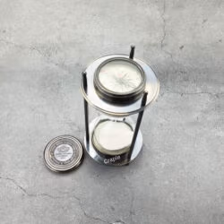 The black antique brass sand timer with one of its removable compasses placed beside it.