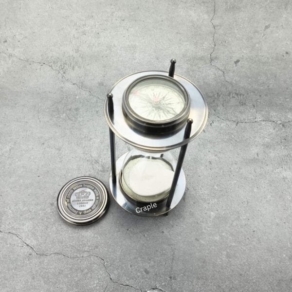 The black antique brass sand timer with one of its removable compasses placed beside it.