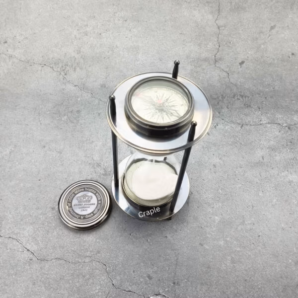 The black antique brass sand timer with one of its removable compasses placed beside it.