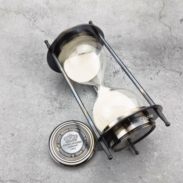 The dual compass sand timer tilted on its side, showing the glass hourglass and black antique finish.