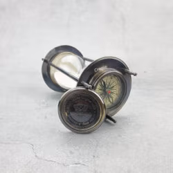 The hourglass sand timer lying on its side with one compass on top and a second detached compass visible.
