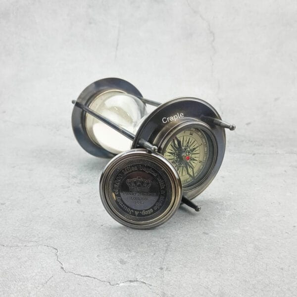 The hourglass sand timer lying on its side with one compass on top and a second detached compass visible.