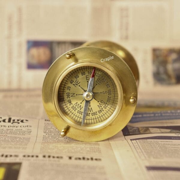 Close-up of the shiny brass functional compass on one end of the hourglass sand timer.