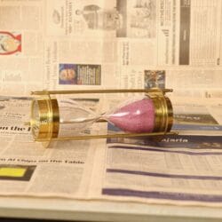 The brass and glass 5-minute sand timer with pink sand, shown lying horizontally.