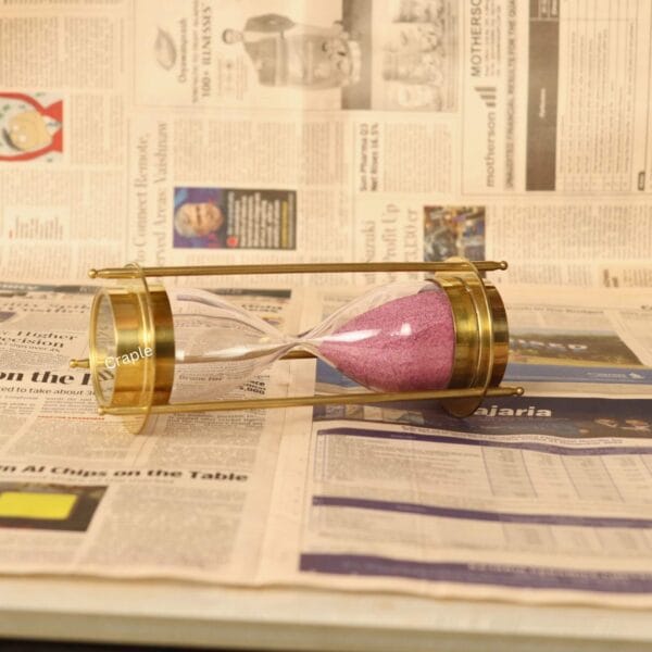 The brass and glass 5-minute sand timer with pink sand, shown lying horizontally.