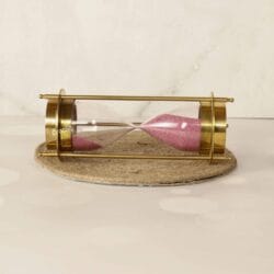 Horizontal view of the dual-compass brass sand timer resting on its rustic jute base.