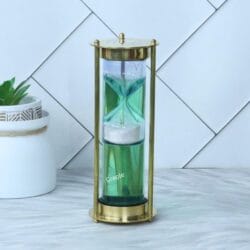 A modern liquid hourglass with a shiny brass frame and white sand suspended inside a green fluid-filled cylinder.