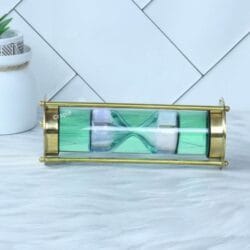 The 1-minute white sand liquid timer viewed horizontally, showcasing its sleek cylindrical design and brass pillars.