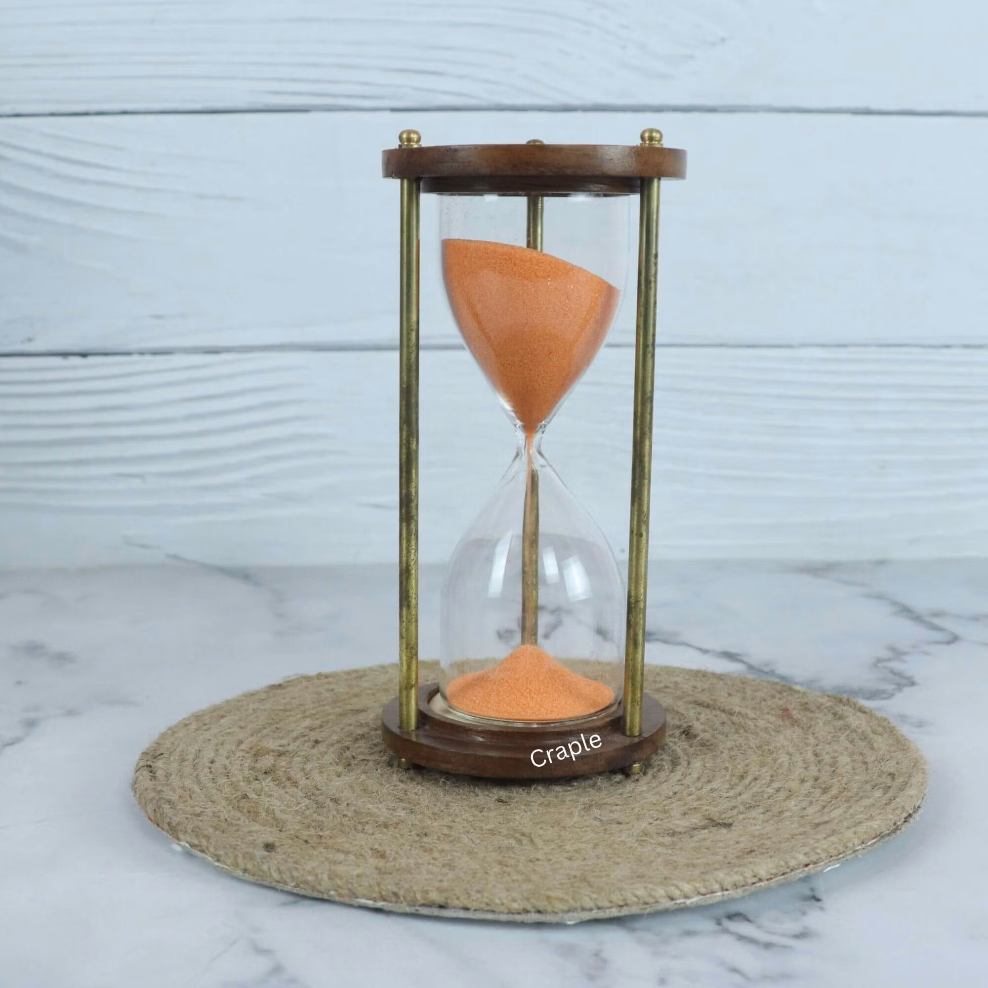 A handcrafted 5-minute hourglass with vibrant orange sand, framed by round wooden bases and shiny brass pillars.