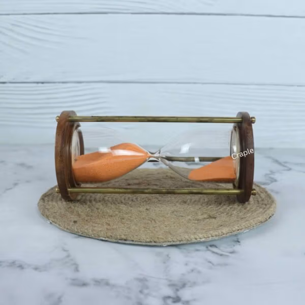 The wood and brass hourglass with orange sand resting horizontally on a jute coaster.