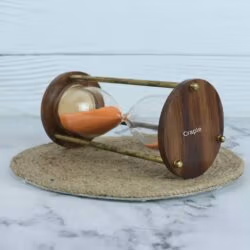 Angled view of the decorative hourglass, showing the rich grain of the wooden base and the brass pillars.