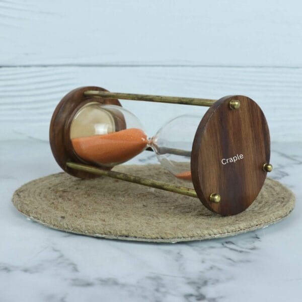 Angled view of the decorative hourglass, showing the rich grain of the wooden base and the brass pillars.