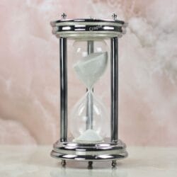 A handcrafted 10-minute hourglass with a polished steel frame, sturdy pillars, and fine white sand.