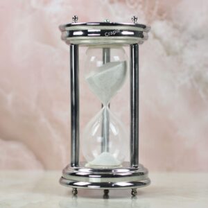 A handcrafted 10-minute hourglass with a polished steel frame, sturdy pillars, and fine white sand.
