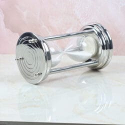 The white sand hourglass viewed from the side while lying down, focusing on the round steel base.